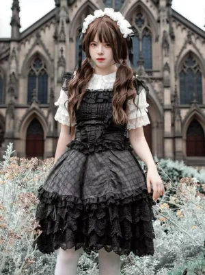 Black Gothic Lolita JSK dress with tiered lace ruffles, plaid jacquard bodice, and square neckline, front full view on model in outdoor church garden setting