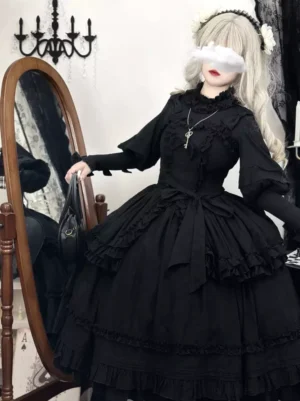 Black Gothic Lolita jumper dress front three-quarter view featuring high ruffled collar, lantern sleeves, layered tiered ruffles, and waist bow detail on model in gothic bedroom setting