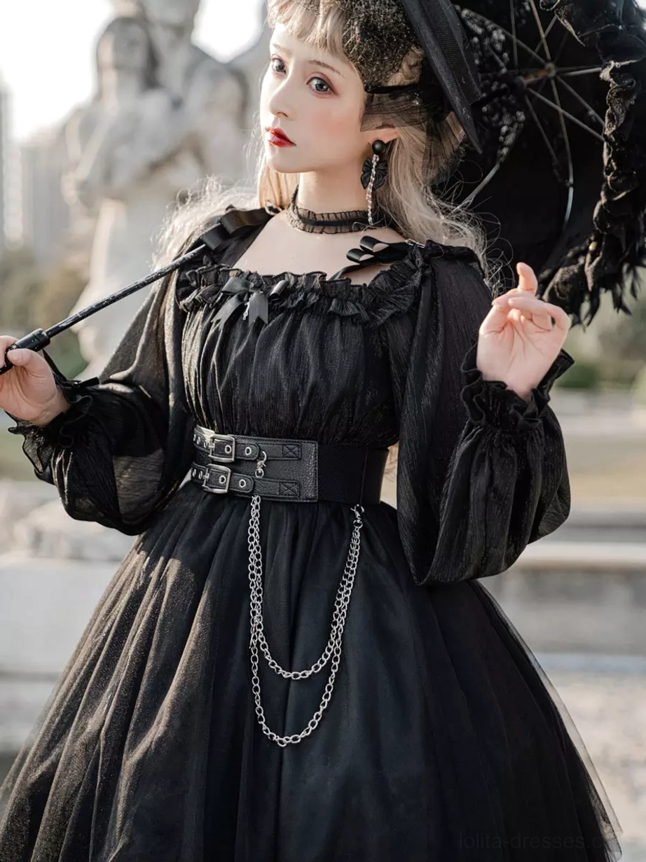 Black Gothic Lolita OP dress close-up front view with gothic stone statue background, showcasing ruffled square neckline, long puff sleeves, dual-chain wide waist belt, model holding black lace parasol