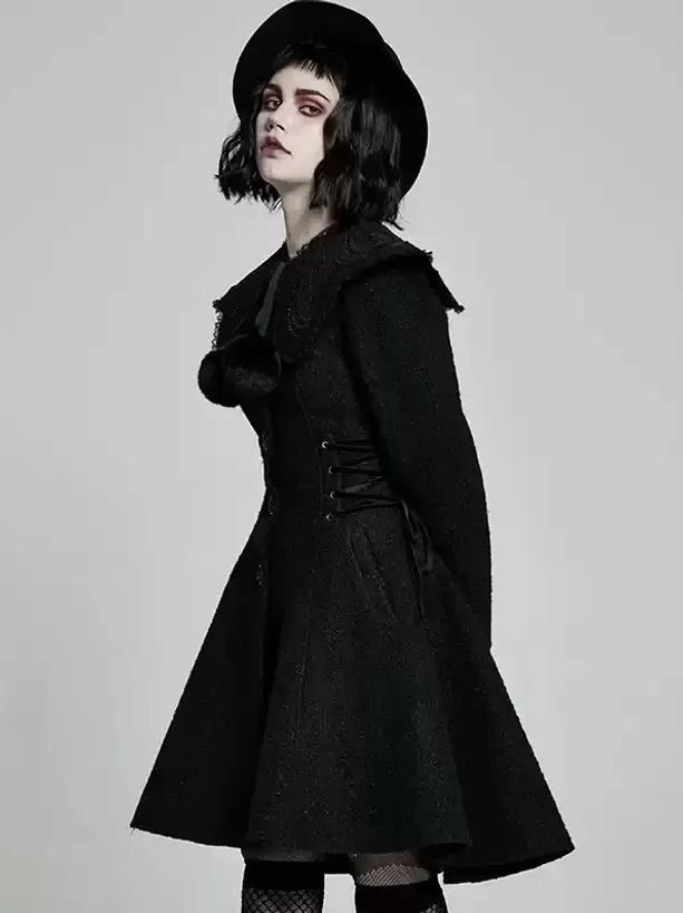 Three-quarter side front angle of black gothic lolita overcoat showing decorative pom-pom on chest, ruffled collar detail, waist lacing, structured silhouette with fedora styling