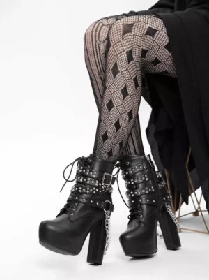 Black Gothic Lolita platform ankle boots with studded straps and hanging chain details, worn with diamond-pattern fishnet tights and black drape skirt, side-front partial view showing lace-up closure