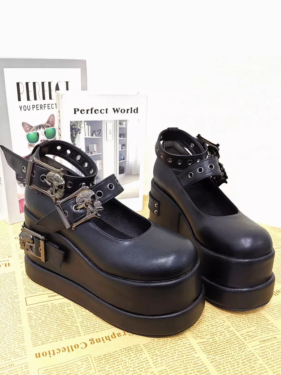 Pair of black Gothic Lolita platform shoes side back three-quarter view on newspaper backdrop featuring eyelet ankle strap dual skull buckles and matte black wedge outsole