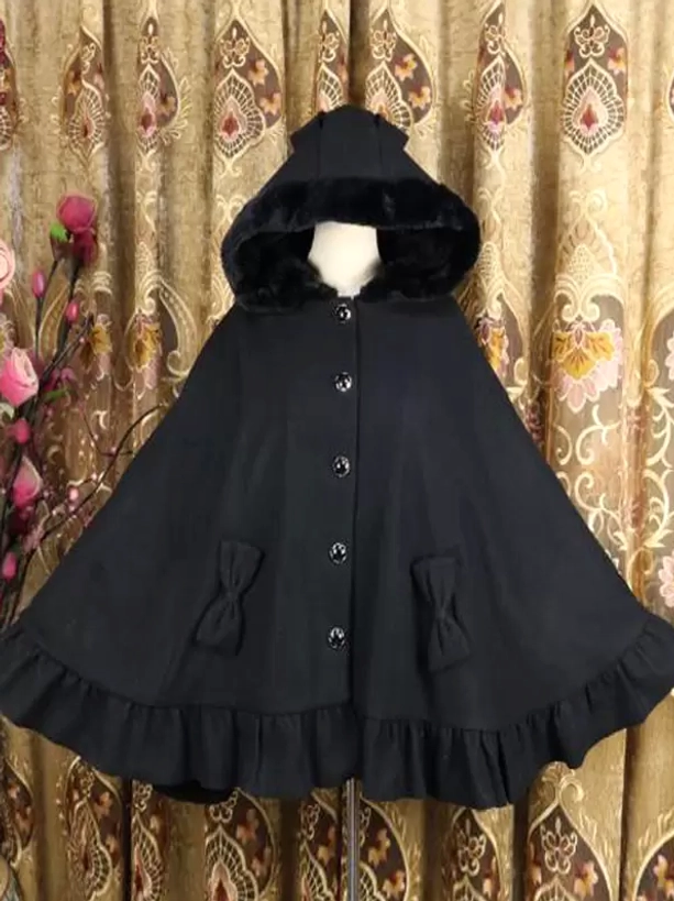 Black Gothic Lolita poncho coat with furry hood, front button closure, and ruffled hem with bow pocket trim details on vintage curtain backdrop