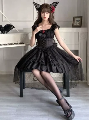 Black Gothic Lolita jumper dress front sitting full-body view featuring corset bodice, layered tulle skirt with red rose lace decoration, and cat ear hairpiece, worn in white piano studio