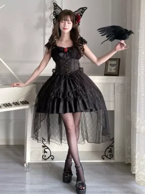Black Gothic Lolita dress front standing full-body shot displaying high-low tulle skirt, corset design, red rose brooch, and crow prop accessory indoors