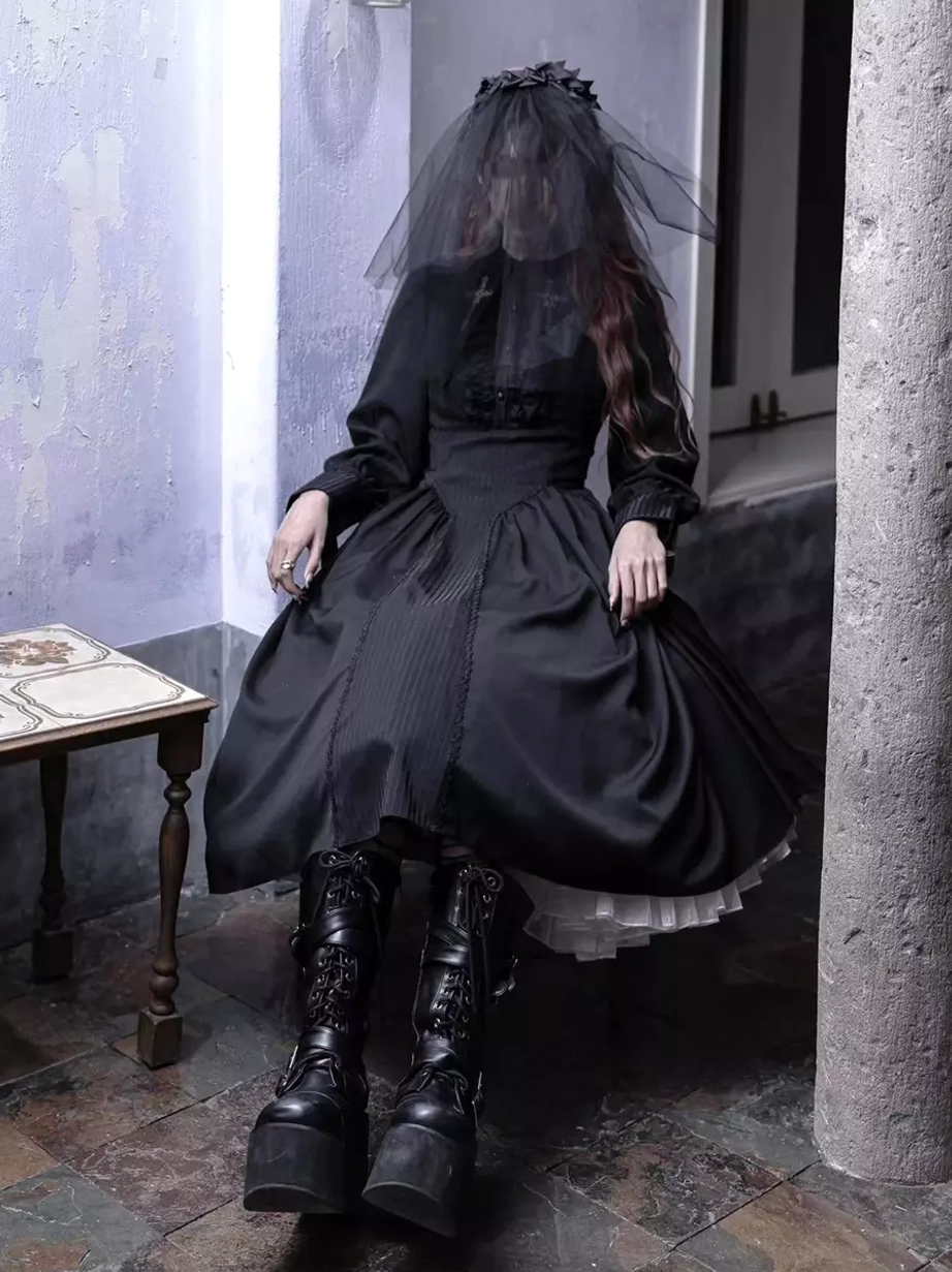 Black Gothic Lolita long sleeve dress low-angle sitting pose, showing high waist, flared midi skirt, long sleeves, sheer veil headdress, and platform combat boots in vintage interior setting