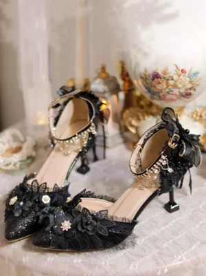 Black Gothic Lolita stiletto heels with glittery upper and 3D flower appliques, displayed from oblique top-down angle on luxury vintage tabletop with decorative elements, showcasing intricate floral toe design and crystal ankle chain strap details