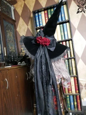 Black gothic lolita witch hat front view with red flower bow and flowing lace veil, mannequin with silver long wig in vintage library backdrop