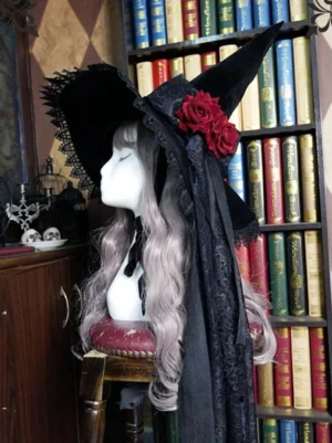 Black gothic lolita witch hat with red rose bow and long lace veil, left side profile view worn on mannequin with silver wig in vintage library setting