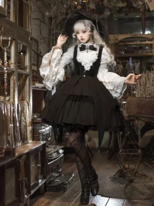 Full front view of black gothic lolita witch outfit featuring the pointed headdress with tiered black skirt, flared lace sleeves, bow necktie, and patterned black stockings in vintage workshop backdrop