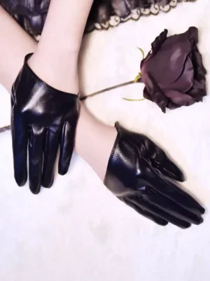 Black glossy PU leather open-back gothic lolita gloves displayed on female forearms against white plush backdrop, showing wrist-exposing cut design and smooth polyurethane finish with dark rose ornament accent, oblique top-down perspective highlighting fashion coordination