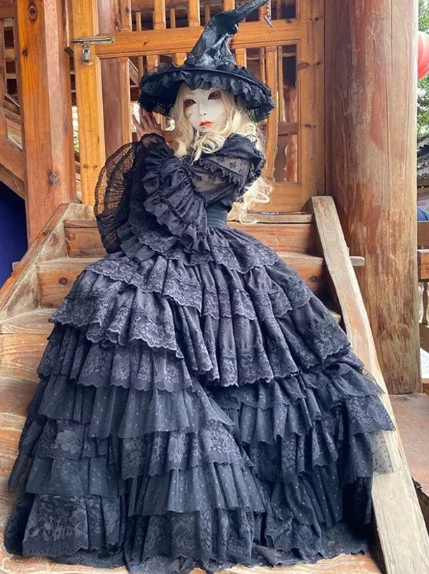 Black Gothic witch lolita dress three-quarter side view on wooden stairs showing ruffled layered skirt and lace details with witch hat