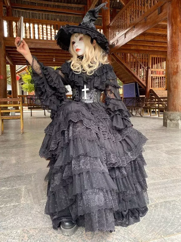 Black Gothic witch lolita dress three-quarter front view with tiered lace skirt worn with witch hat and cross corset decoration