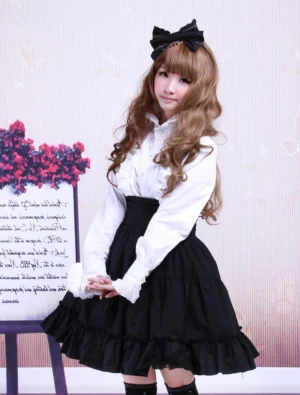 Black high-waist tiered ruffles Gothic Lolita skirt front three-quarter view on model with curly brown hair wearing black bow accessory and Victorian-inspired styling with floral display background