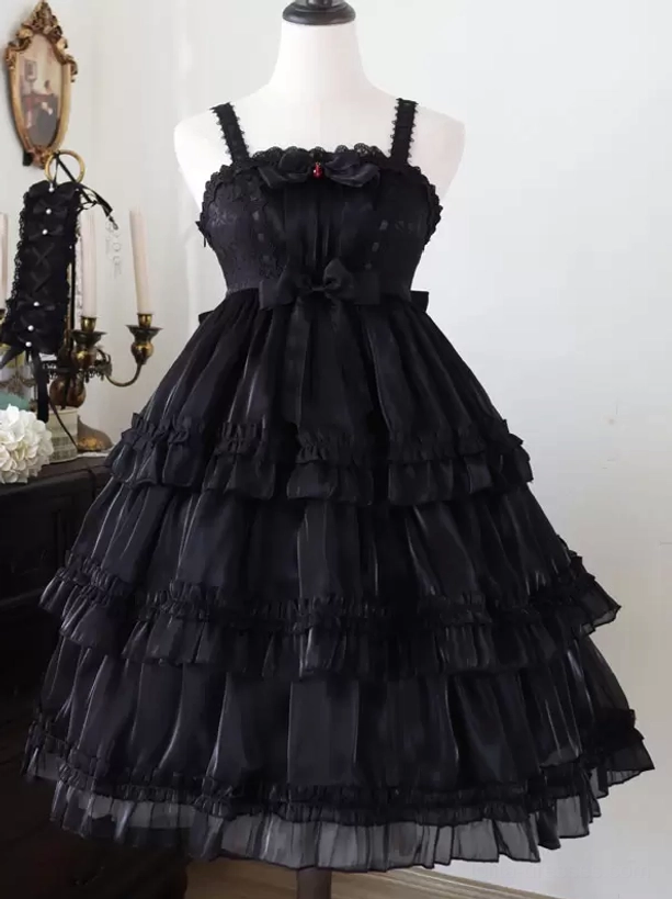 Black sweet Hime Lolita jumper dress front full view with chest bow decoration, tiered ruffled glossy black skirt, elegant silhouette in vintage indoor setting