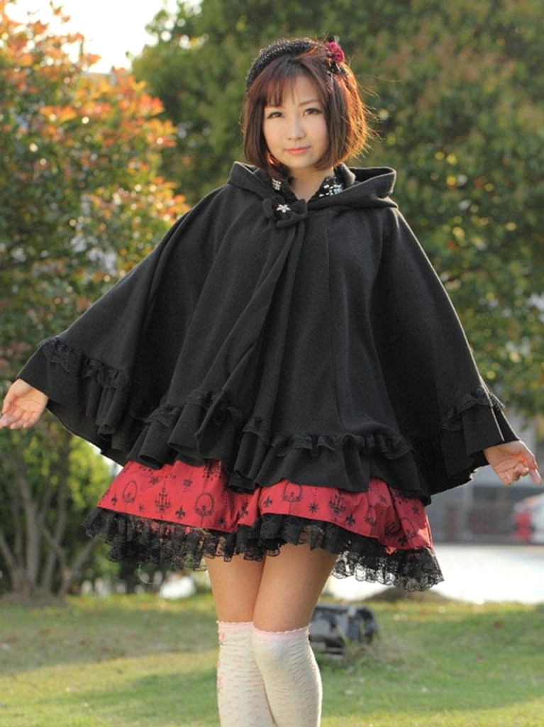 Outdoor park setting showing black hooded lolita cape coat full-body shot with ruffled hem and wide flared sleeves