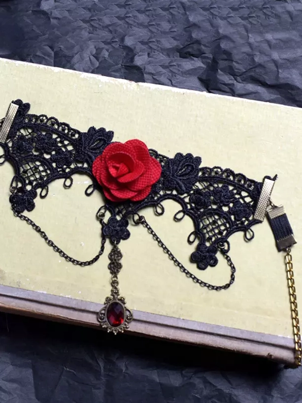 Black lace gothic arm cuff with adjustable metal strap system and central red gem dangling chain on vintage book, flat lay styling shot