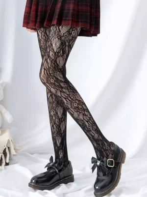 Classic black lace fishnet Lolita tights showcasing intricate vine flower design, paired with red plaid skirt and black Mary Jane shoes, front side angle on white fabric