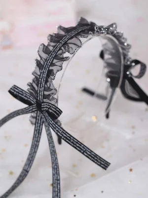 Black lace lolita headband flat lay display showing intricate ruffled lace detailing and printed ribbon bow with flowing tails on starry background