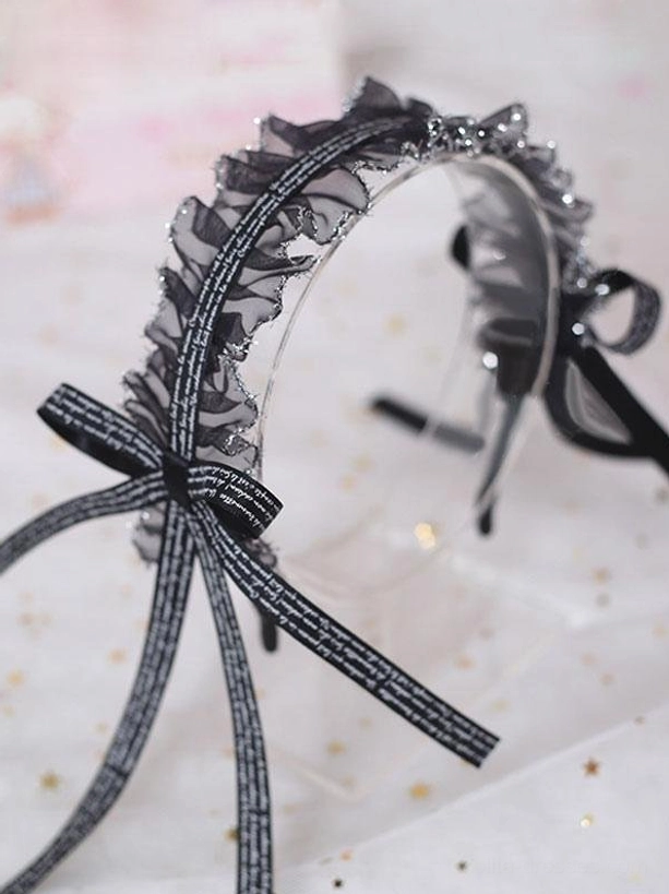 Black lace lolita headband flat lay display showing intricate ruffled lace detailing and printed ribbon bow with flowing tails on starry background