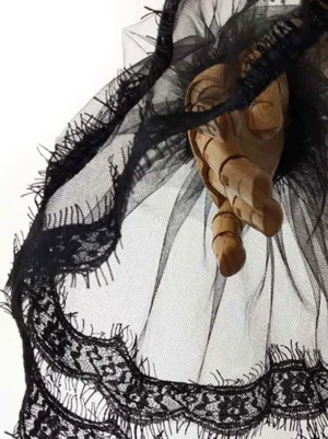 Single black lace wrist cuff close-up side view on wooden mannequin hand showing sheer mesh layered lace edging frayed details