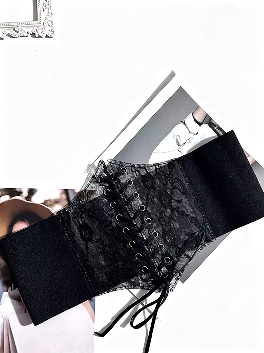 Black lace waist cincher with metal eyelet lace-up design and sheer floral lace detailing, shown at angle with vintage magazine props and decorative frame styling for gothic lolita coordination inspiration