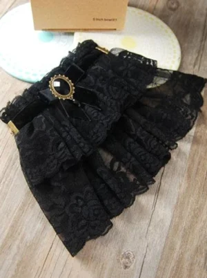 Black lace wrist cuffs with double ruffled floral lace and vintage gem brooch displayed on wooden table with decorative tray and packaging box overhead view