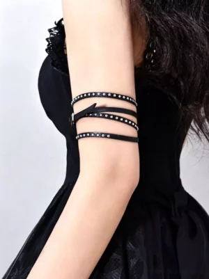 Black leather studded arm band with silver rivets worn on female model wearing gothic black dress, rear side close-up view showing multi-layer strap construction and adjustable metal buckle design