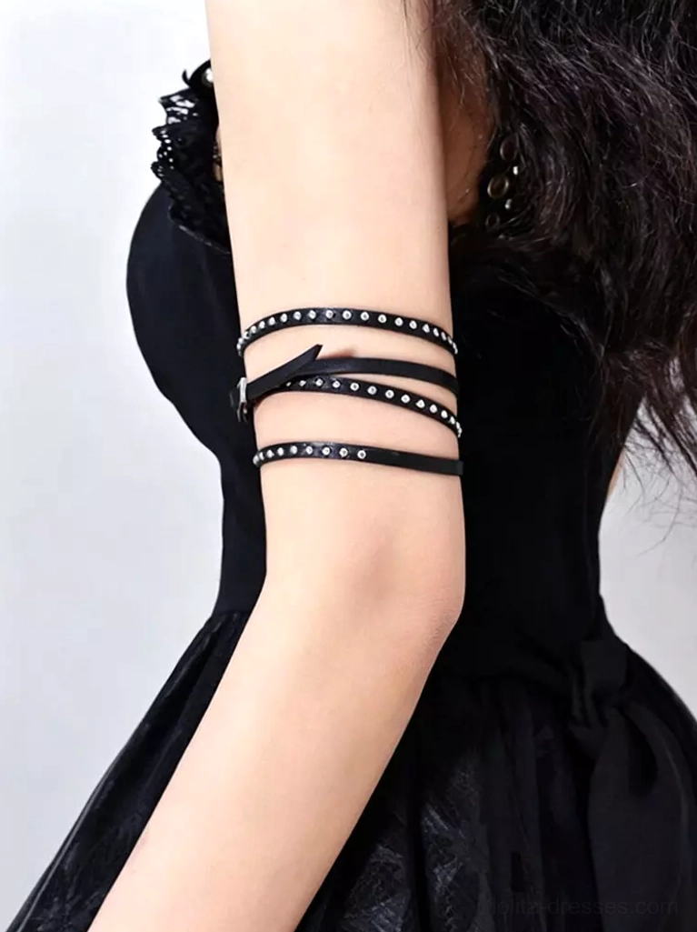 Black leather studded arm band with silver rivets worn on female model wearing gothic black dress, rear side close-up view showing multi-layer strap construction and adjustable metal buckle design