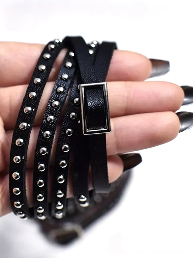 Black leather arm strap with square metal buckle and silver studs close-up on female hand with dark nail polish, handheld photography showing craftsmanship detail