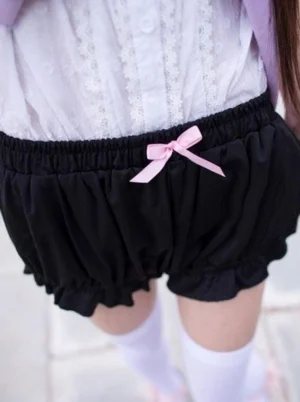 Black cotton lolita bloomers shorts with pink bow detail and ruffled hem back partial view paired with white lace blouse and thigh-high socks