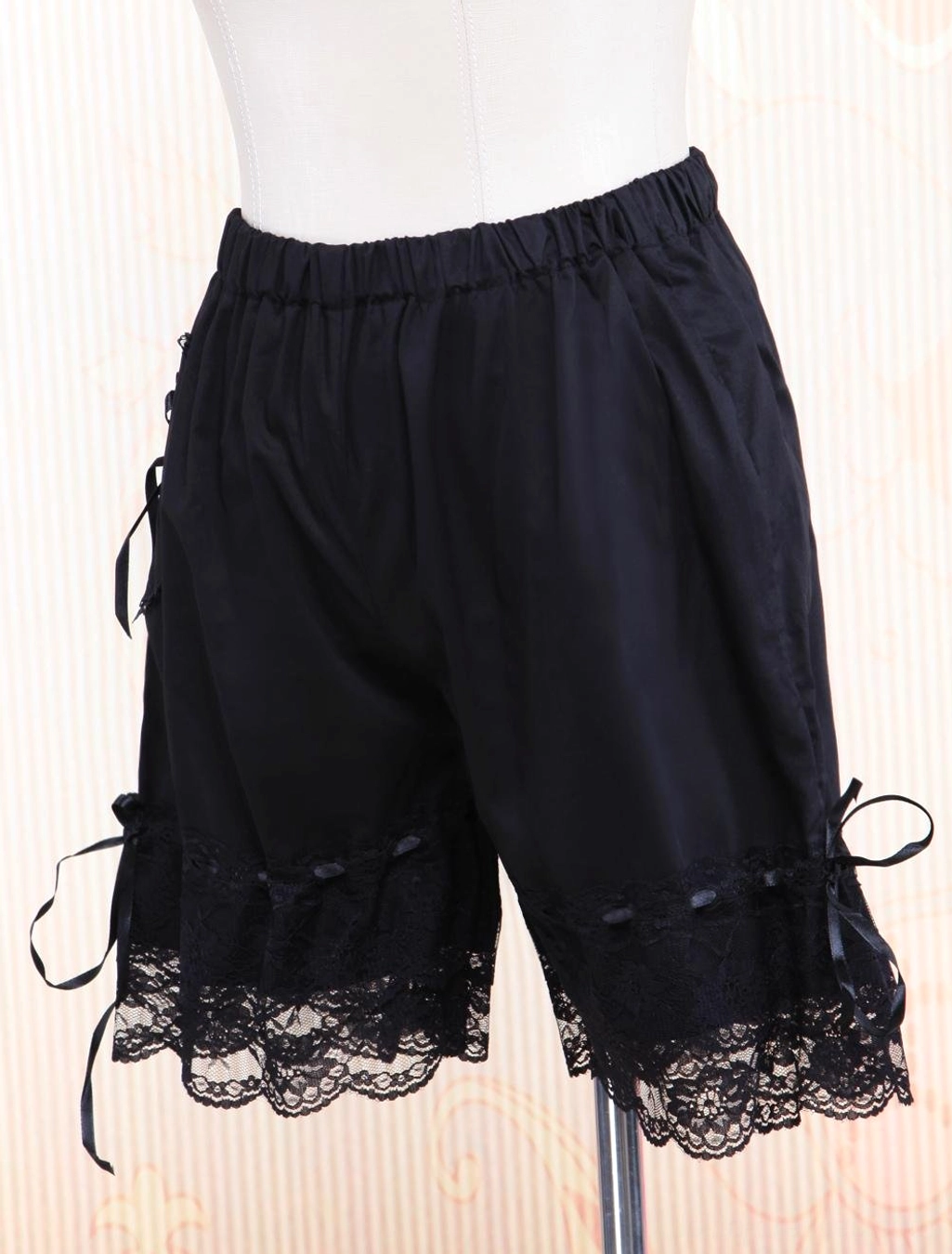 Black lolita bloomer shorts right side profile displaying ruffled lace hem, satin ribbon ties, and solid black cotton fabric construction on display stand