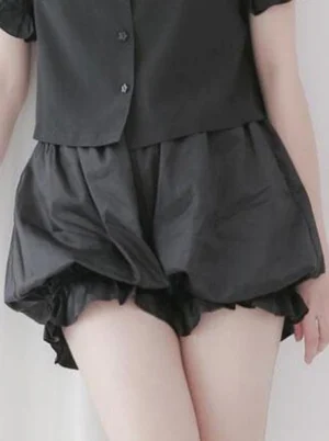 Black lolita cotton bloomer shorts with ruffled elastic leg cuffs and gathered waist, styled with black cropped button shirt, front view displaying puffy balloon silhouette and hem ruffles