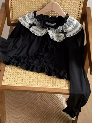 Black lolita crop shrug flat lay on rattan chair showing double lace collar tiny bow accents and ruffle hemline details sweet lolita outerwear