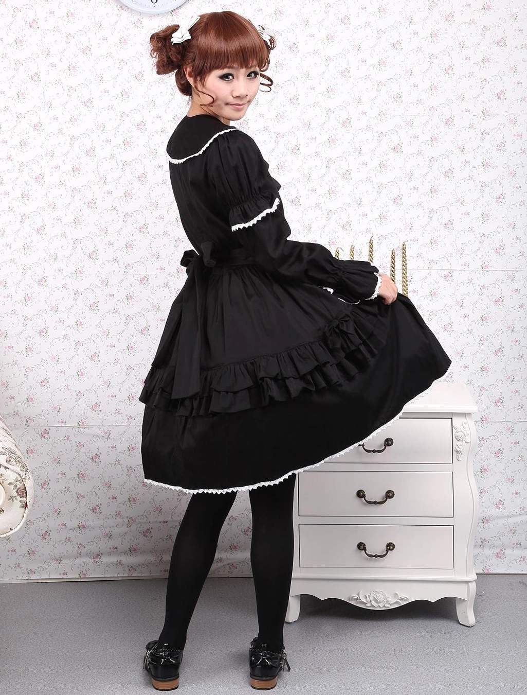 Back view of model wearing black Lolita dress showing back waist bow detail and lace-trimmed layered ruffled skirt hem