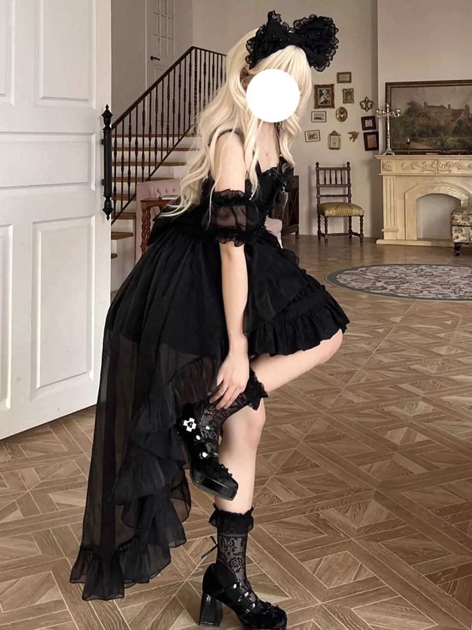 Side full-body view of black gothic lolita dress with off-shoulder puff sleeves short puffy skirt and long sheer tulle train worn with heeled boots and lace socks