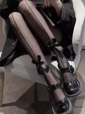 Black lolita fishnet tights with bow ankle decoration worn with black Mary Jane shoes and black coat, showing mesh texture and vertical leg seam detail in close-up lower limb shot