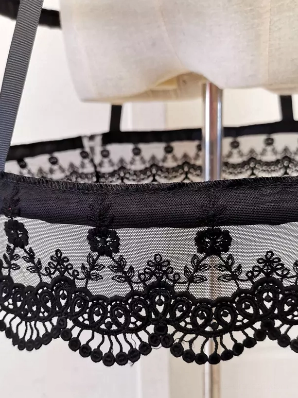 Close-up overhead view of black Lolita petticoat scalloped lace hem with tassel-like edge detail on black mesh and lace base fabric