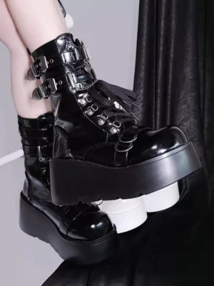 Close-up side view of black platform ankle boots with metal buckles fringe trim and glossy chunky platform sole against dark fabric backdrop