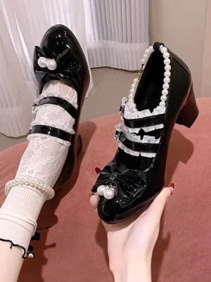Black lolita platform heels close-up detail shot showing heart-shaped buckles pearl beaded trim cascading ruffle straps and pearl bow pendant charm against pink backdrop on-foot