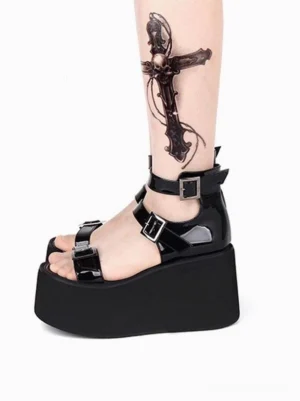 Black patent lolita platform sandal side view on model leg, featuring glossy finish, ankle buckle strap, toe buckle fastening, chunky black wedge platform sole, open round toe design