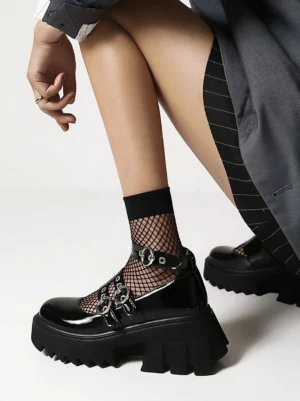 Black lolita platform shoes side view while sitting, shiny PU leather with double buckle straps and thick jagged platform sole, formal casual styling