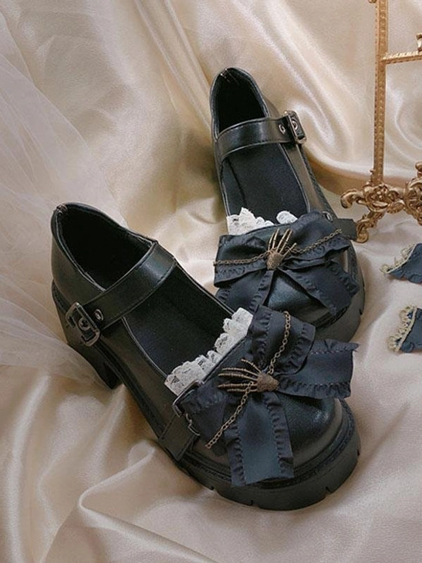Black Lolita platform shoes three-quarter flat lay with skeleton hand bow, lace trim, buckle ankle strap, and thick platform sole on satin cloth with golden decor