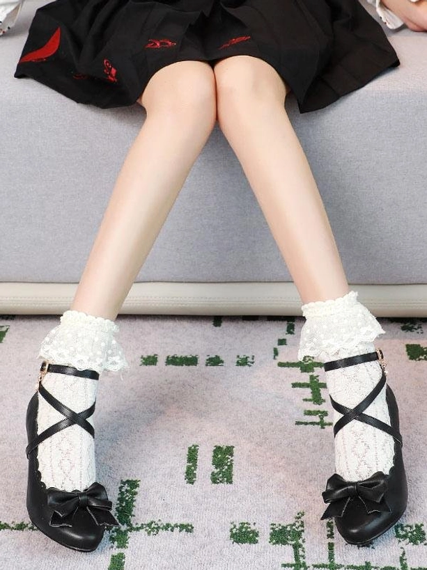 Black lolita prism heel shoes front view seated model wearing ruffled socks and black short skirt showing cross ankle straps