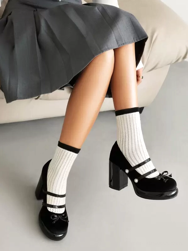 Black Lolita pumps crossed feet side view on sofa background with pleated grey skirt white socks bow strap design