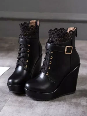 Black lolita platform wedge boots flat lay frontal view displaying black lace collar, gold metal eyelets, and structured wedge sole with marble floor background