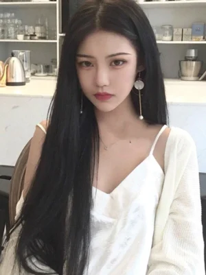 Black long straight lolita wig with center parting on young female model wearing gothic lolita style, indoor bar setting with modern counter background, full front view showcasing smooth jet-black synthetic hair texture