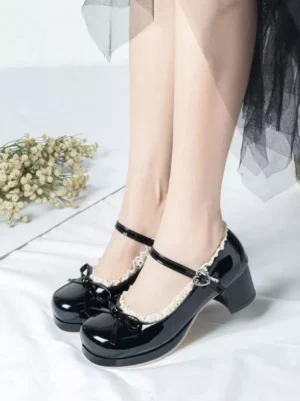 Black glossy Mary Jane Lolita high heels with buckle ankle strap, lace trim and bow accent, front view on model wearing white linen with dried flowers