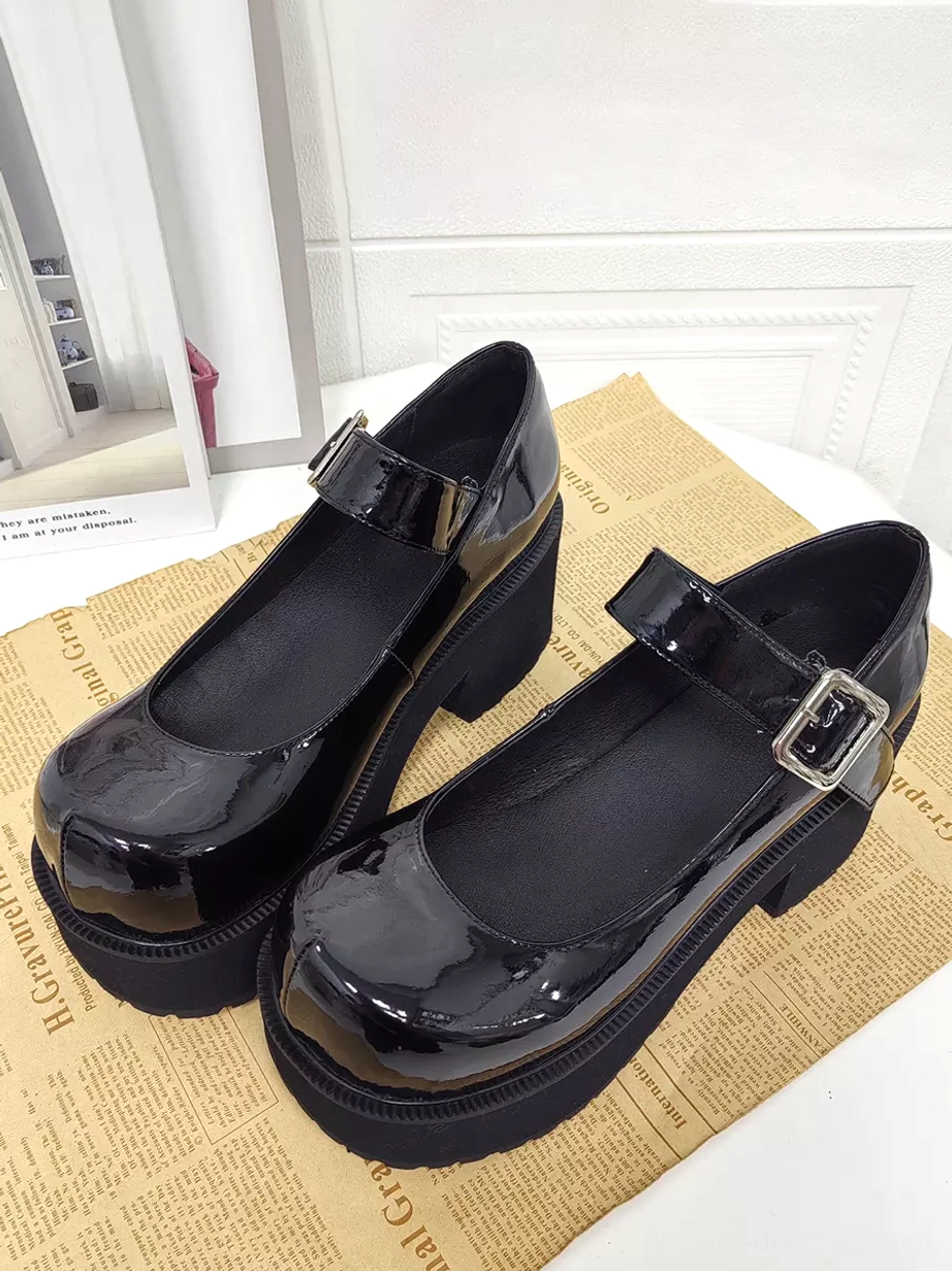 Pair of black patent leather Mary Jane platform heel lolita shoes with shiny round closed toe and block heel displayed in flat top-front view on newspaper surface