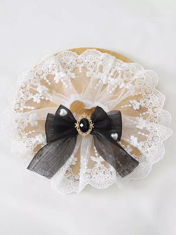 Black organza wrist bow lolita accessory displayed on wooden round base with gold-framed black gemstone and circular embroidered pearl lace